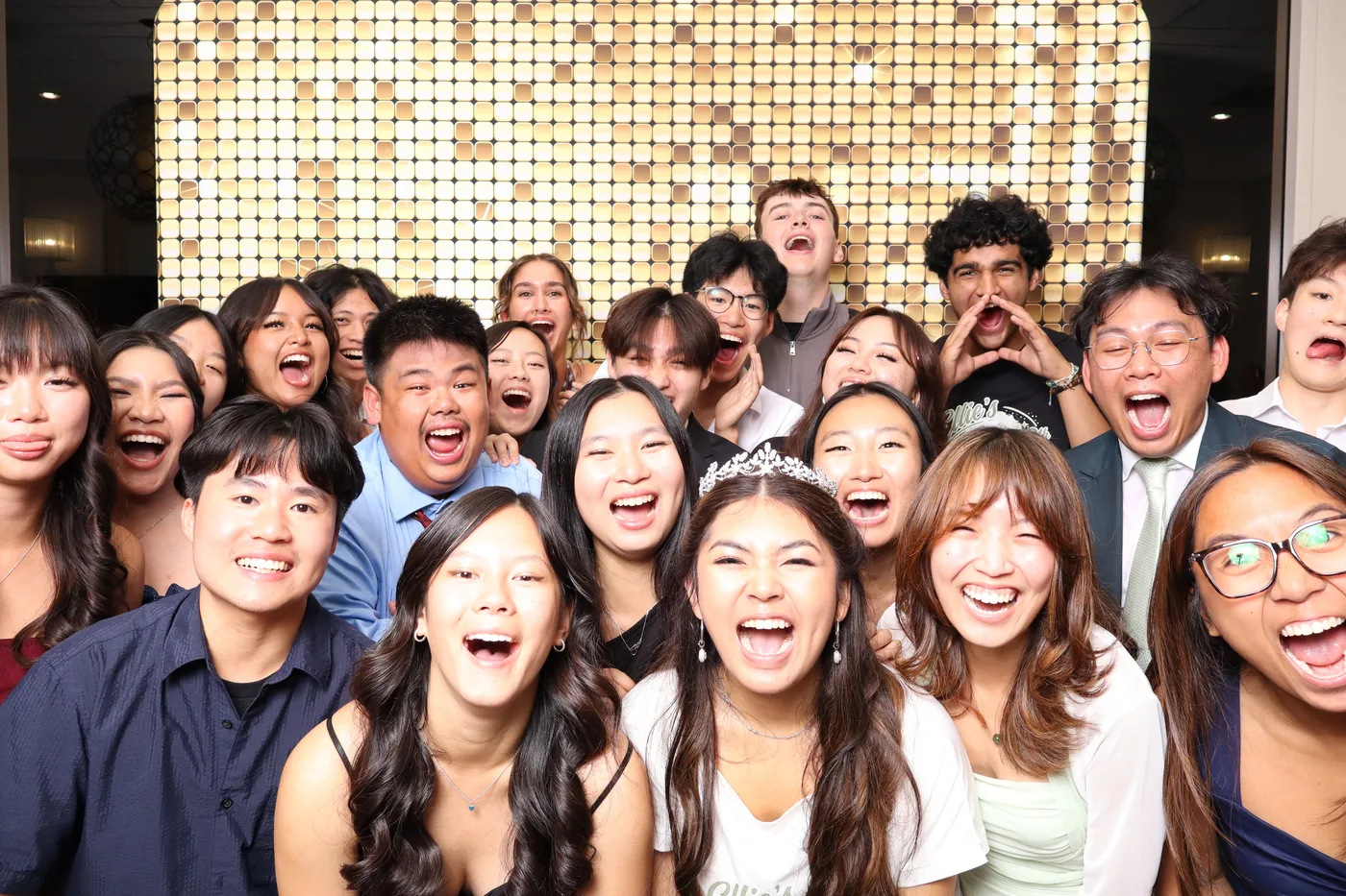 A joyful group cheering together in front of a gold photo booth backdrop