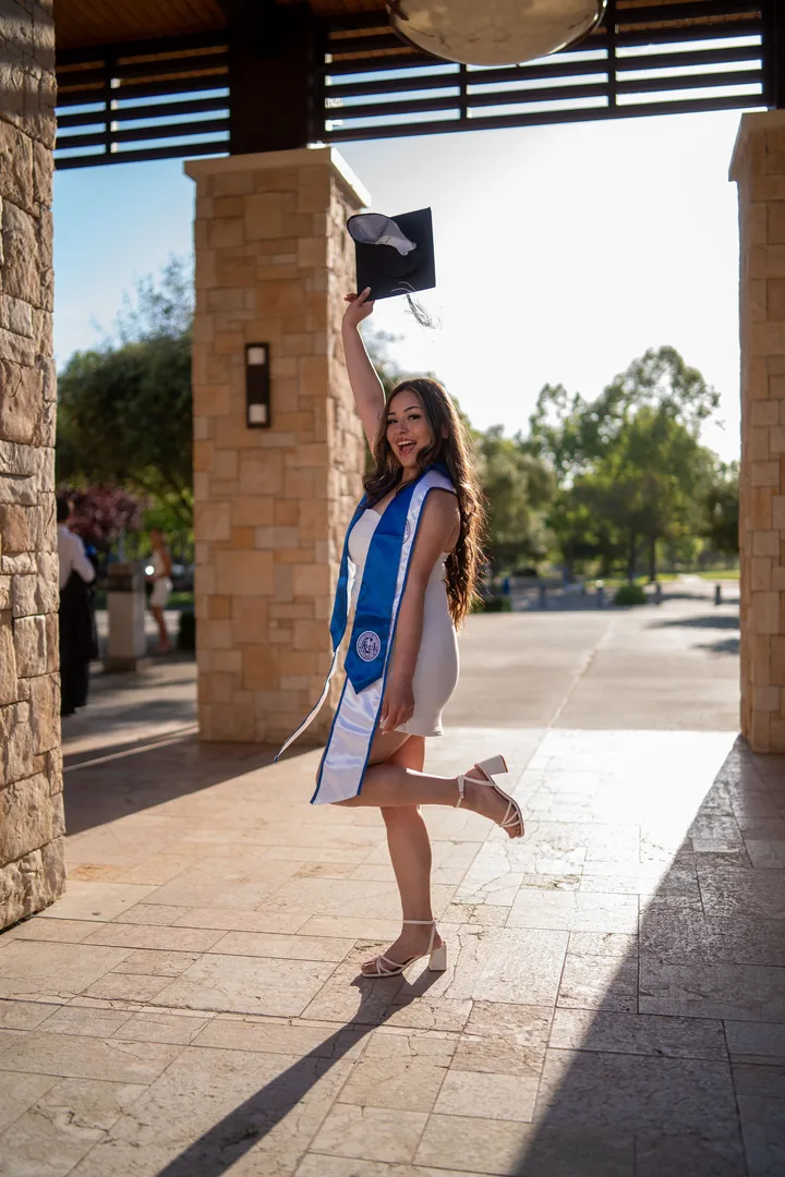 Graduate in cap, gown and sash standing beneath a stone arch